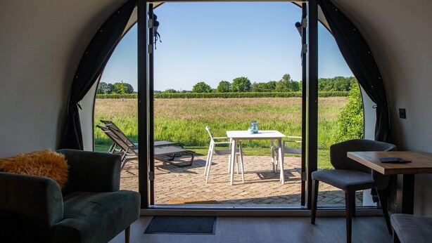 A room with a large arched window, a table with chairs, and a sofa. - Unique Nature Lodge With Terrace Garden (Dalerveen)