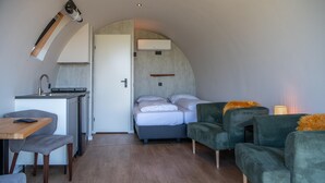 A compact room with a kitchenette, a bed with pillows, and two green armchairs. - Unique Nature Lodge With Terrace Garden (Dalerveen)