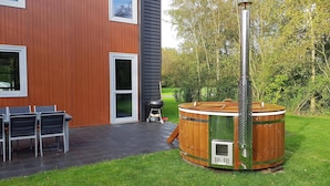 A modern building with a wooden exterior, a patio with chairs, and a hot tub. - Lakeside Luxury; Sauna & Hot Tub (Noordwolde)