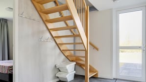 A modern interior with a wooden staircase, a bed with a striped bedspread, a white trash bin, and a glass door leading outside. - Lakeside Luxury; Sauna & Hot Tub (Noordwolde)