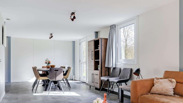 A modern living room with a sofa, a coffee table, and a dining area with a table and chairs. - Lakeside Luxury; Sauna & Hot Tub (Noordwolde)
