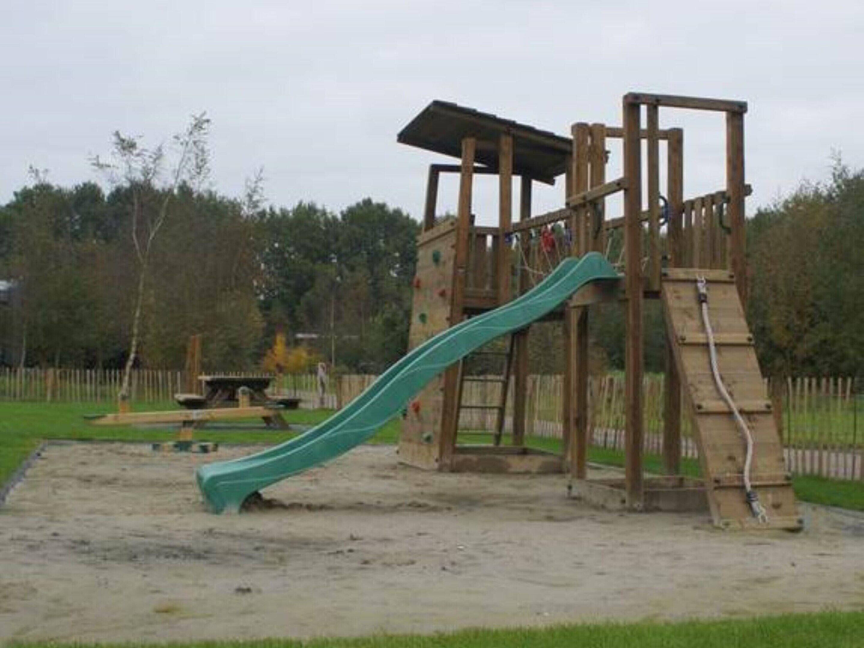 Eine Holzspielanlage mit Rutsche und Kletterelementen in einem Park.