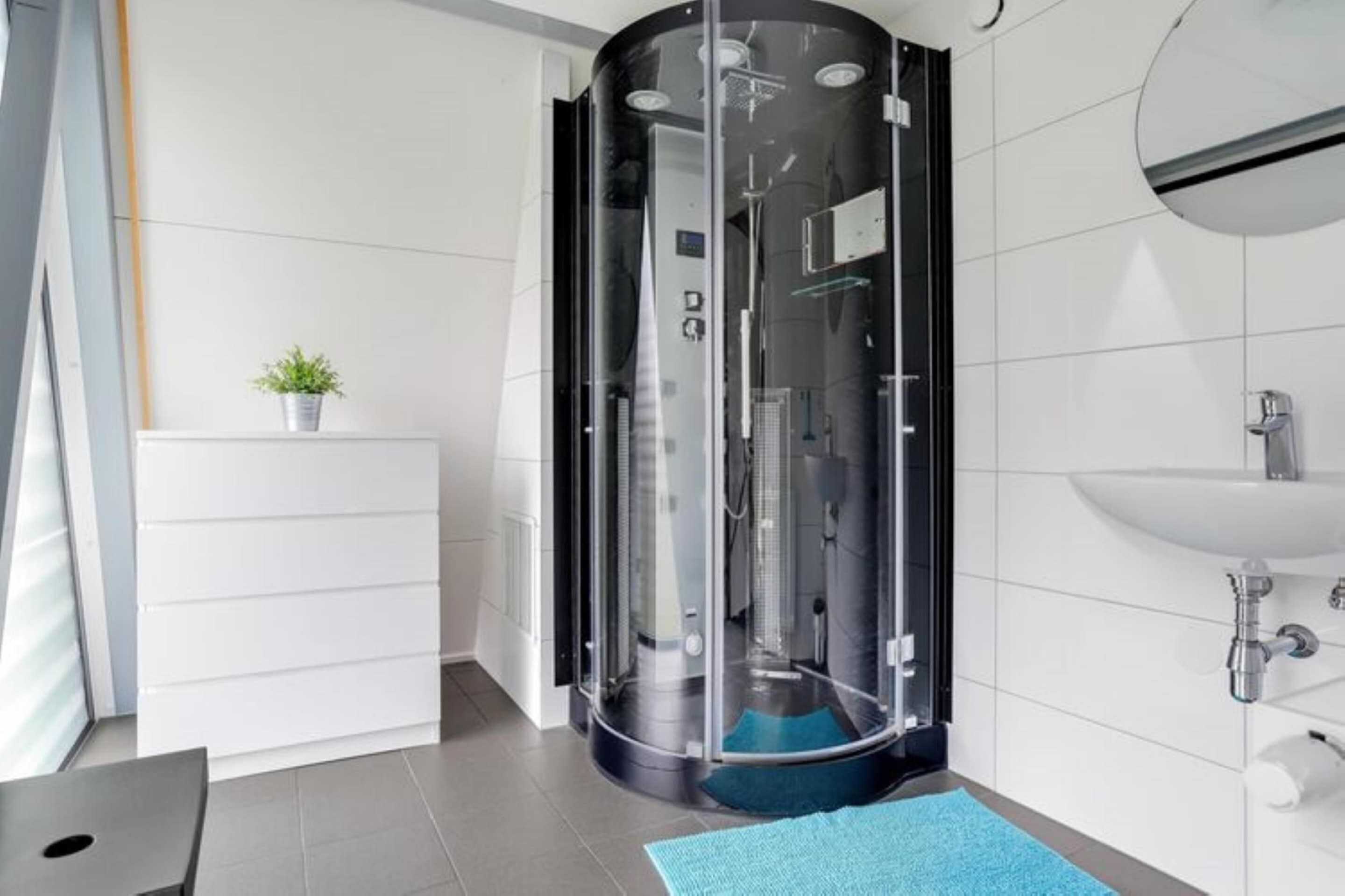 Une salle de bain moderne avec une douche à parois de verre, un lavabo blanc et une petite plante en pot posée sur un meuble.