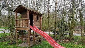 A wooden playhouse with a red slide in a park. - Spacious Holiday Home in Noordwolde With Garden (Noordwolde)