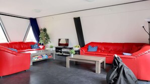 A modern living room with red leather sofas, a coffee table, a TV, and a potted plant. - Spacious Holiday Home in Noordwolde With Garden (Noordwolde)