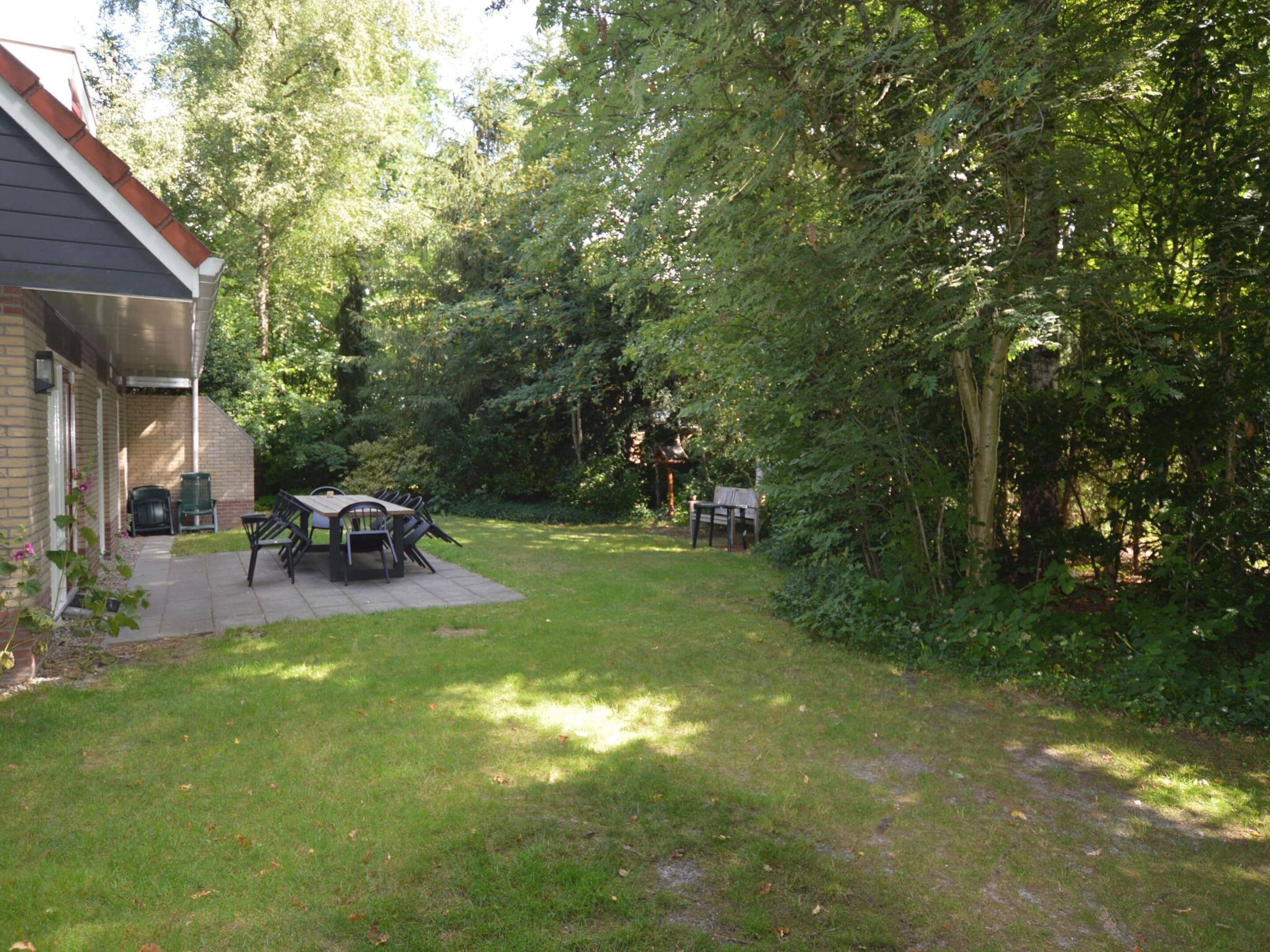 A patio with a table and chairs, surrounded by a lush garden and trees.