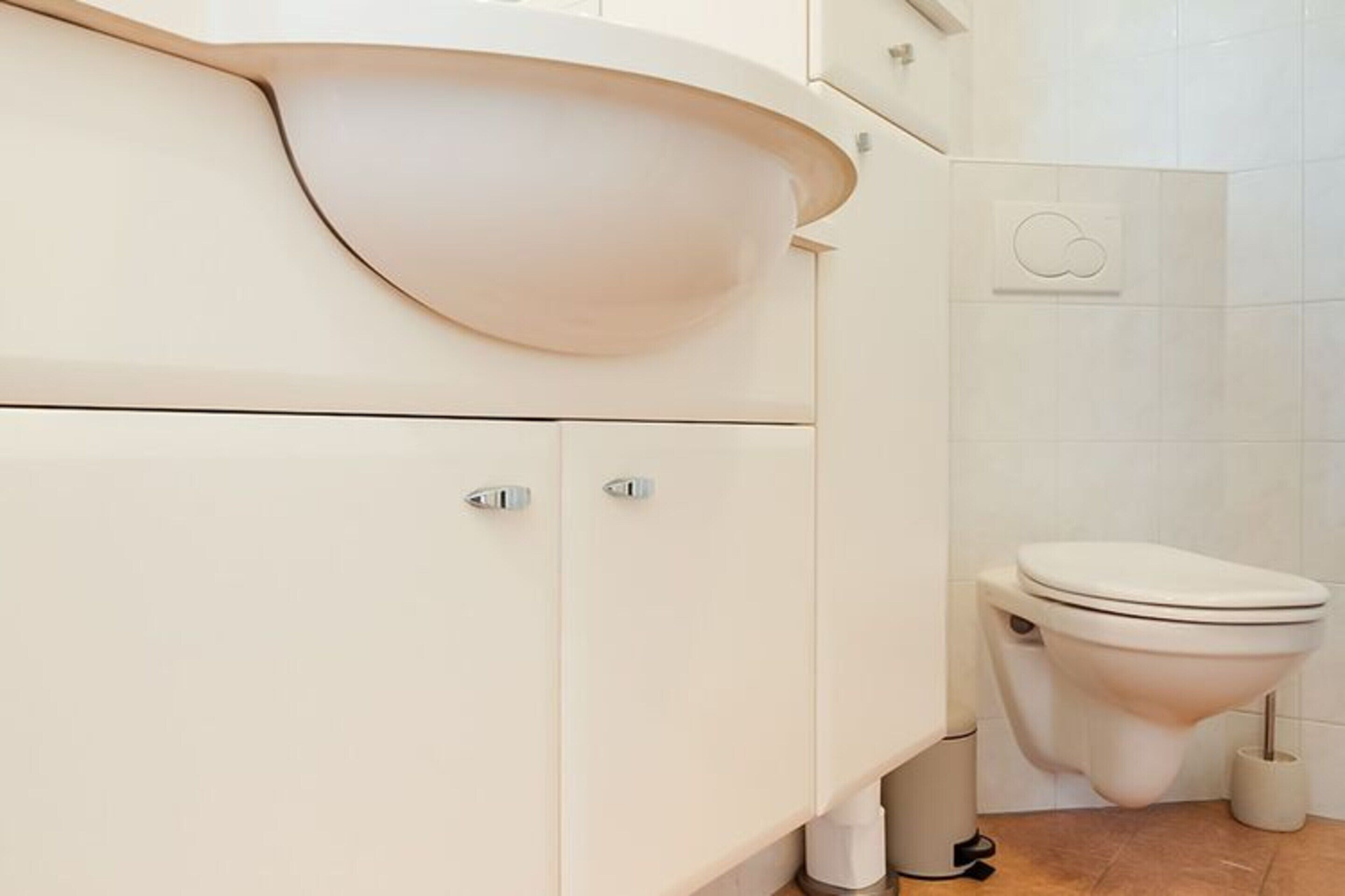 A modern bathroom with a curved sink, a toilet, and a trash bin.