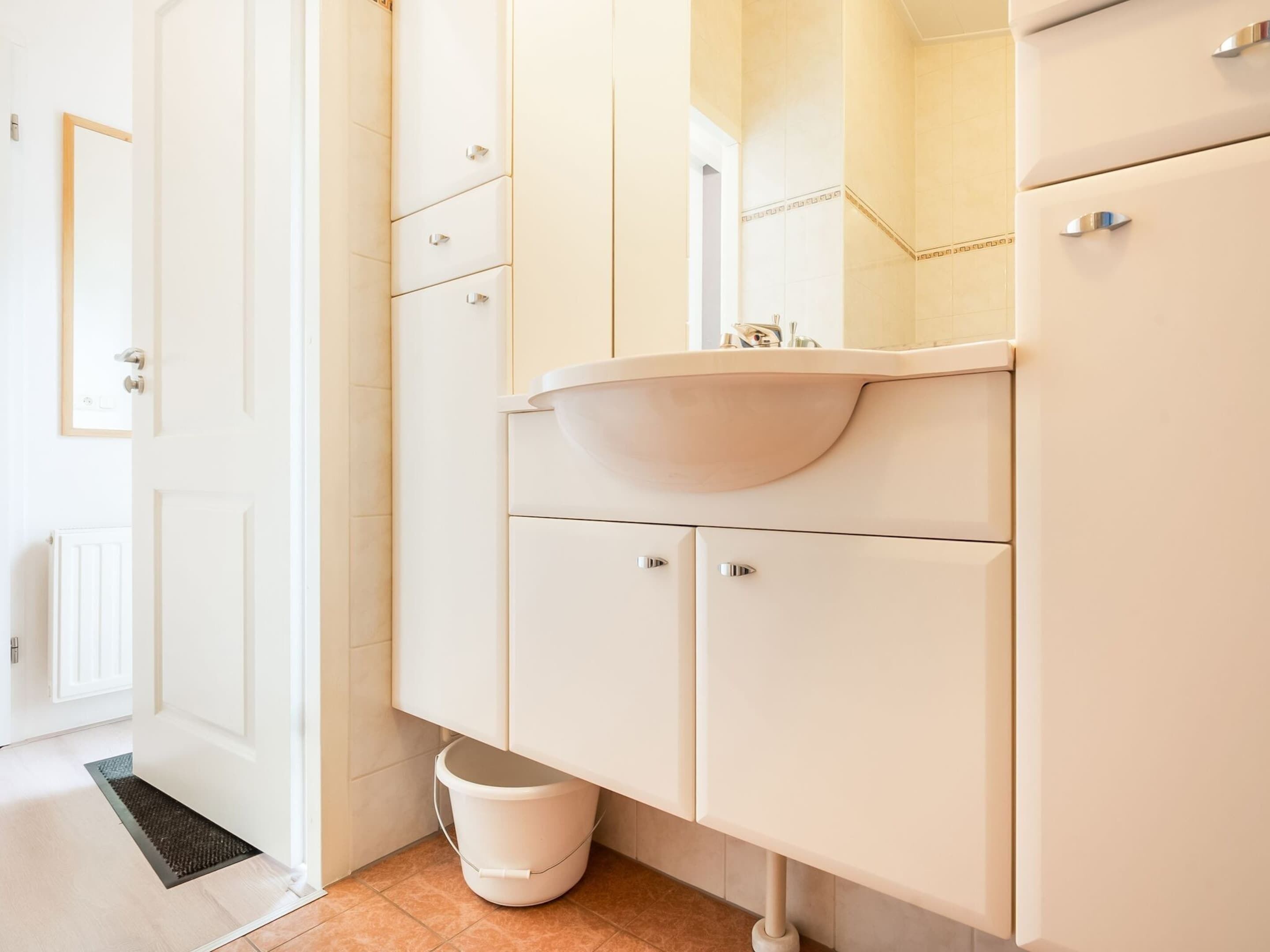 A modern bathroom with a white sink, mirror, and cabinets.