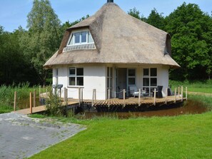 A thatched-roof house with a dock, surrounded by greenery.