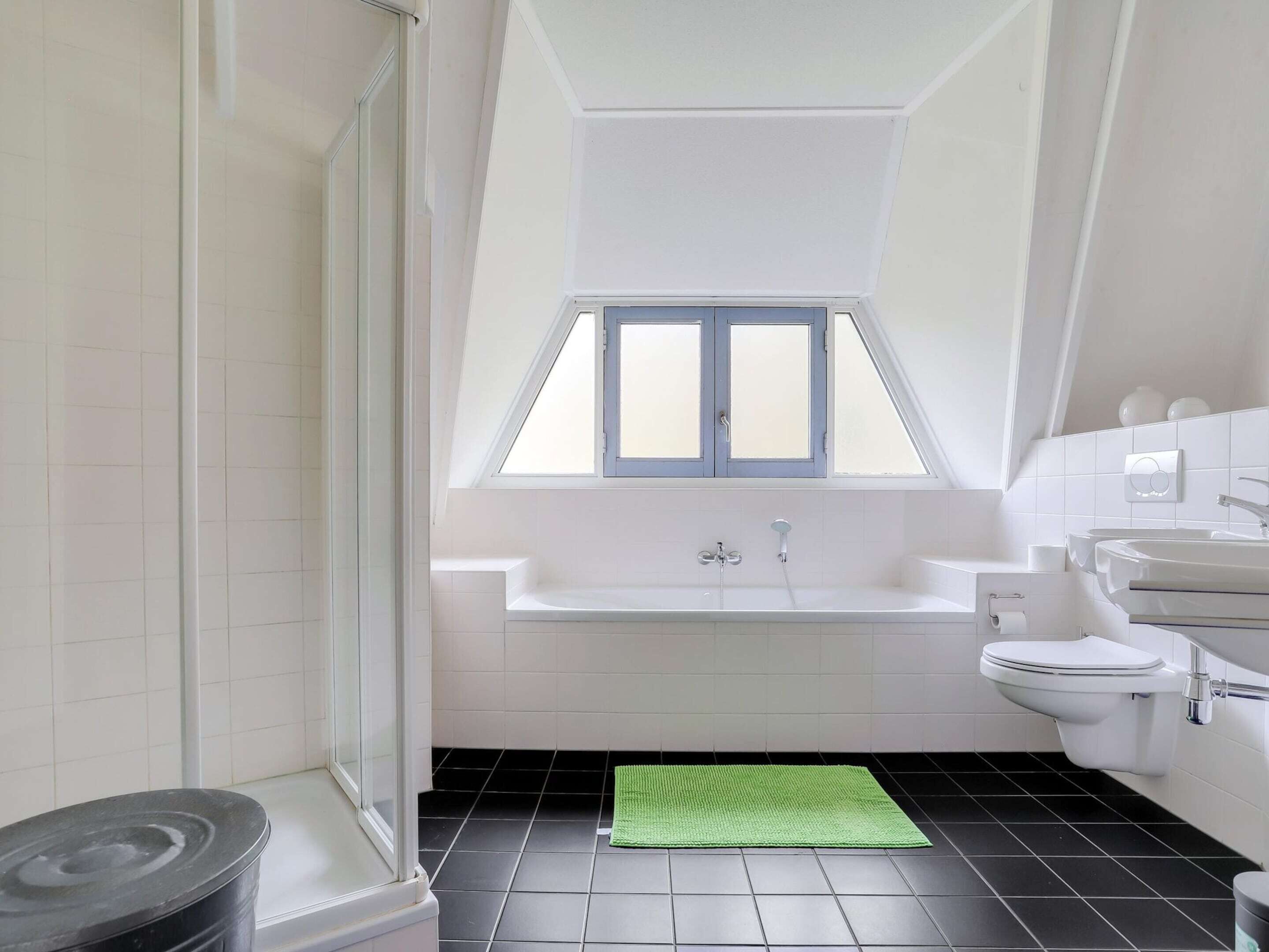 A modern bathroom with a skylight, a bathtub, a toilet, and a sink.