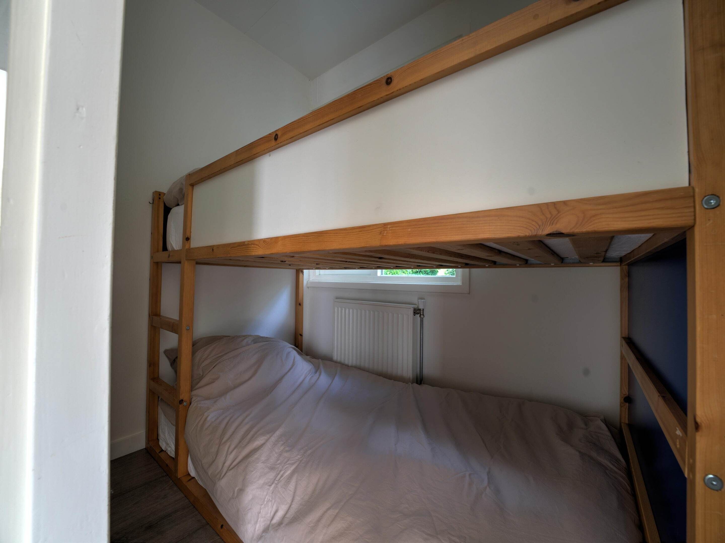 A bunk bed with a wooden frame, a ladder, and a window above the lower bunk.