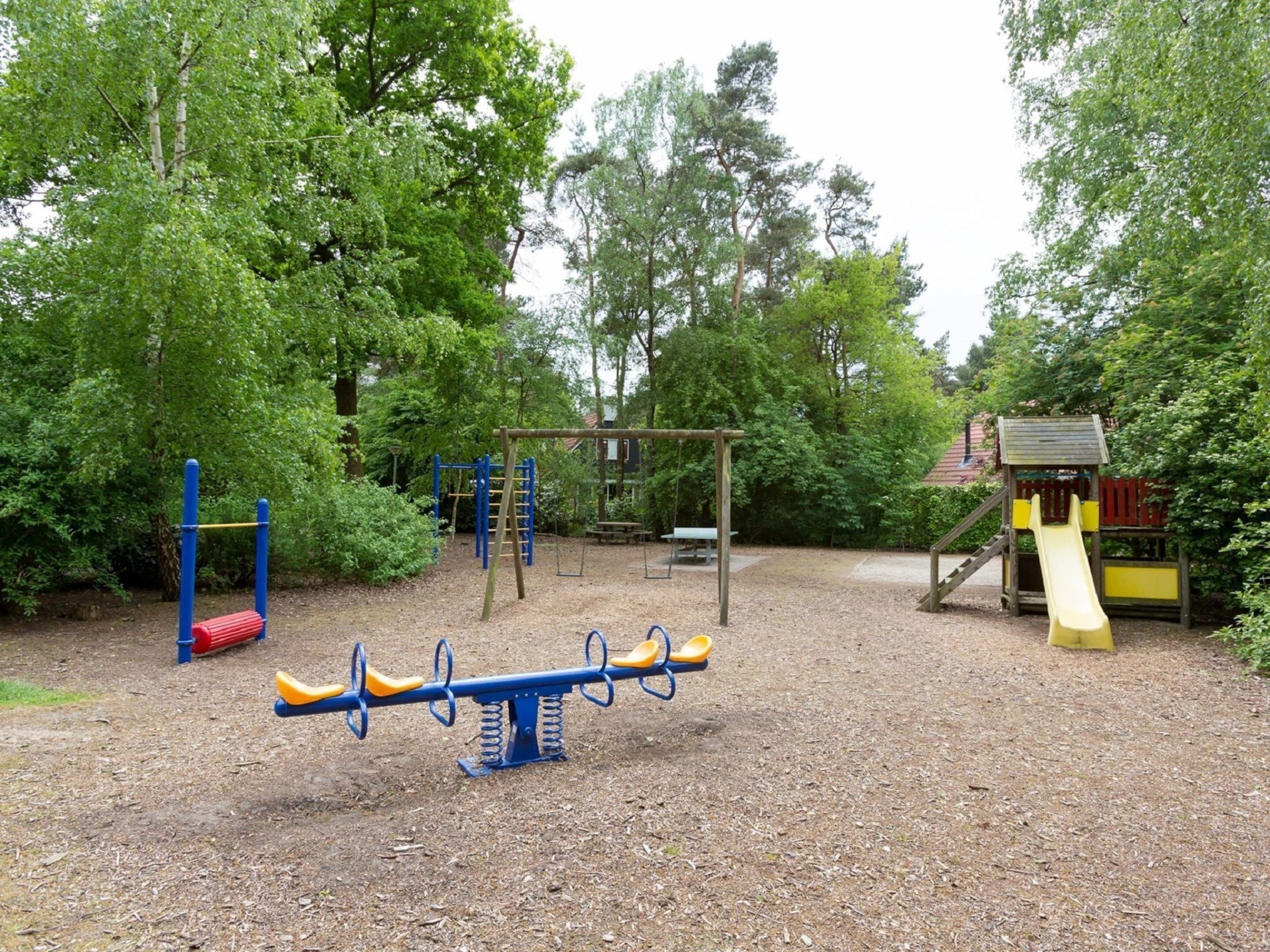 A playground with a seesaw, climbing structures, and a slide.