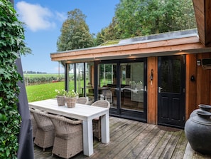 A modern outdoor dining area with a white table and wicker chairs, overlooking a lush garden and a field. - Fantastic Chalet Near Open Waterways, hot tub (Rutten)