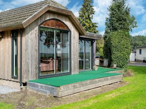 A wooden house with large windows, a green outdoor area, and a tall tree. - Fantastic Chalet Near Open Waterways, hot tub (Rutten)