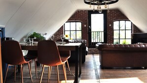 A dining area with a brick wall, a large window, and a ceiling fan. - Shed 57b in an old Flour Mill in Haulerwijk (Haulerwijk)