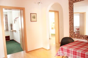 Una habitación con una cama, una mesa con mantel a cuadros, un espejo con marco de madera y una puerta que da a otra estancia.