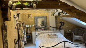 A bedroom with a sloped ceiling, a bed with a floral bedspread, a chair, and a mirror on the wall. - La Chenaie ( 2C ) (Sorges et Ligueux en Périgord)