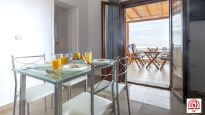 A dining area with a glass table and chairs, breakfast items, and a view through an open door to an outdoor patio. - Villa Naya (Santorini)