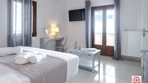 A hotel room with a bed, a desk, a TV, and a view of the outdoors. - Villa Naya (Santorini)