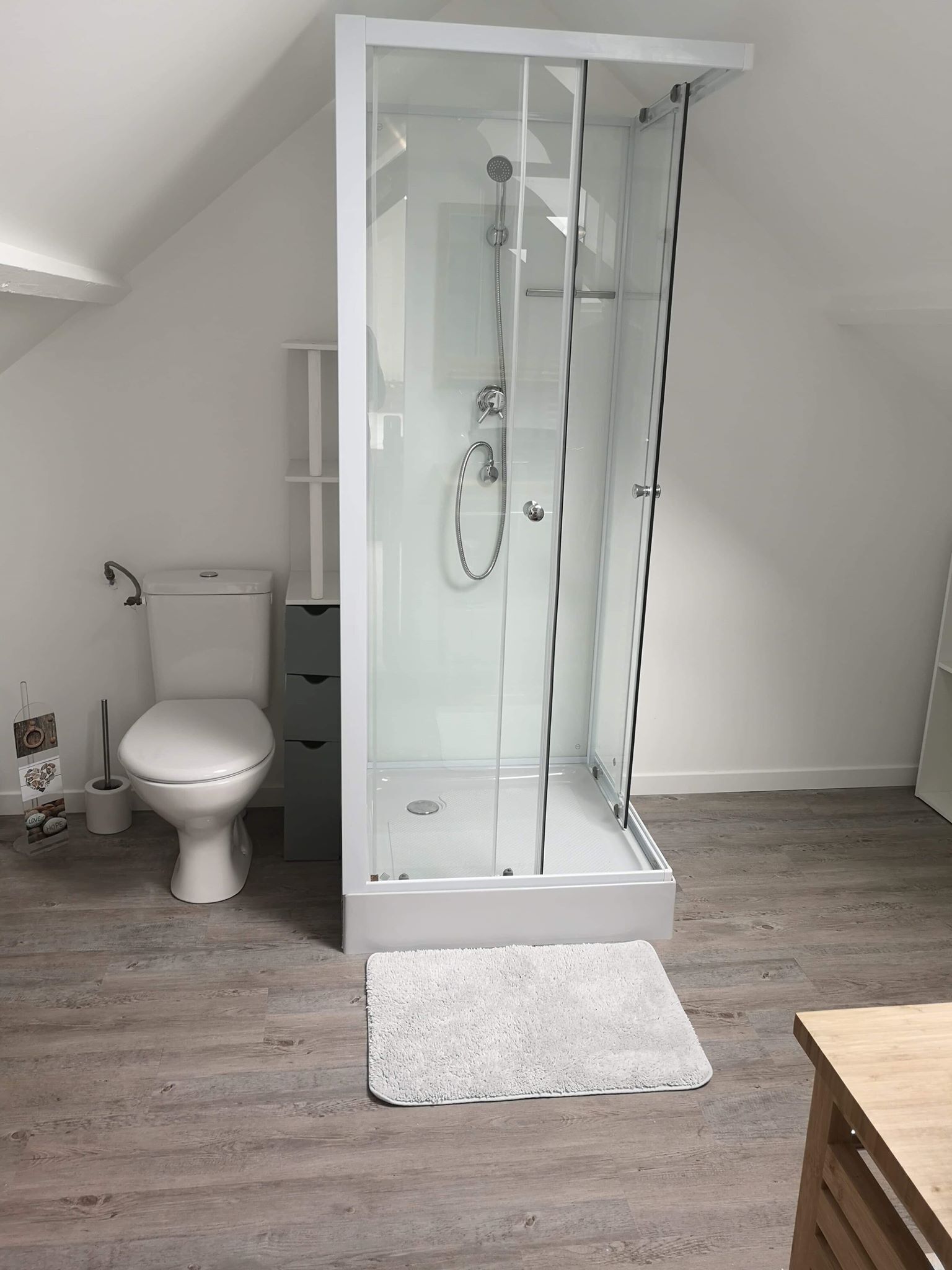 Un bagno moderno con cabina doccia in vetro, un water e pavimento in legno.