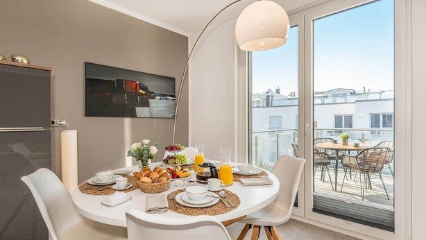 Een moderne eethoek met een ronde tafel, witte stoelen en een groot raam met uitzicht op de stad.