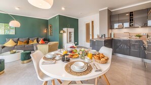 Een moderne woonkamer met een ontbijt klaar gezet tafel, een keuken met donkere kasten, en een groene accentmuur.