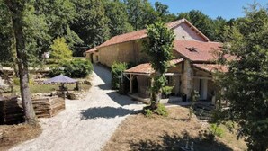 Una casa de pedra amb teulada de rajola, envoltada d'arbres i un camí de grava.