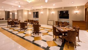 A spacious dining area with multiple tables and chairs, a patterned floor, and wall-mounted lighting. - Rawla Sagrun (Kumbhalgarh)
