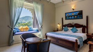 A hotel room with a large bed, a desk, and a window with curtains. - Rawla Sagrun (Kumbhalgarh)