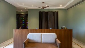 A reception area with a wooden desk, a two-seater sofa, and a ceiling fan. - Rawla Sagrun (Kumbhalgarh)