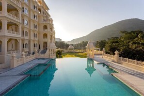 A pool with a reflection of a multi-story building with balconies and a dome structure in the background. - Rawla Sagrun (Kumbhalgarh)