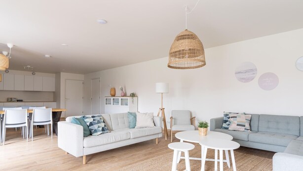 Ett modernt vardagsrum med en soffa, två vita soffbord och en matplats med stolar.