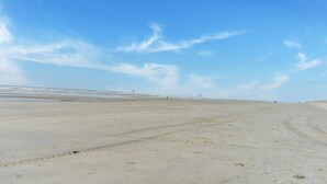 En bred, öppen strand med klar himmel och avlägsna byggnader i horisonten.