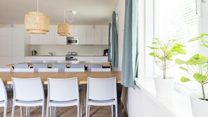 Ett modernt kök med vita skåp, ett matbord i trä och två hängande ljuskronor av rotting.