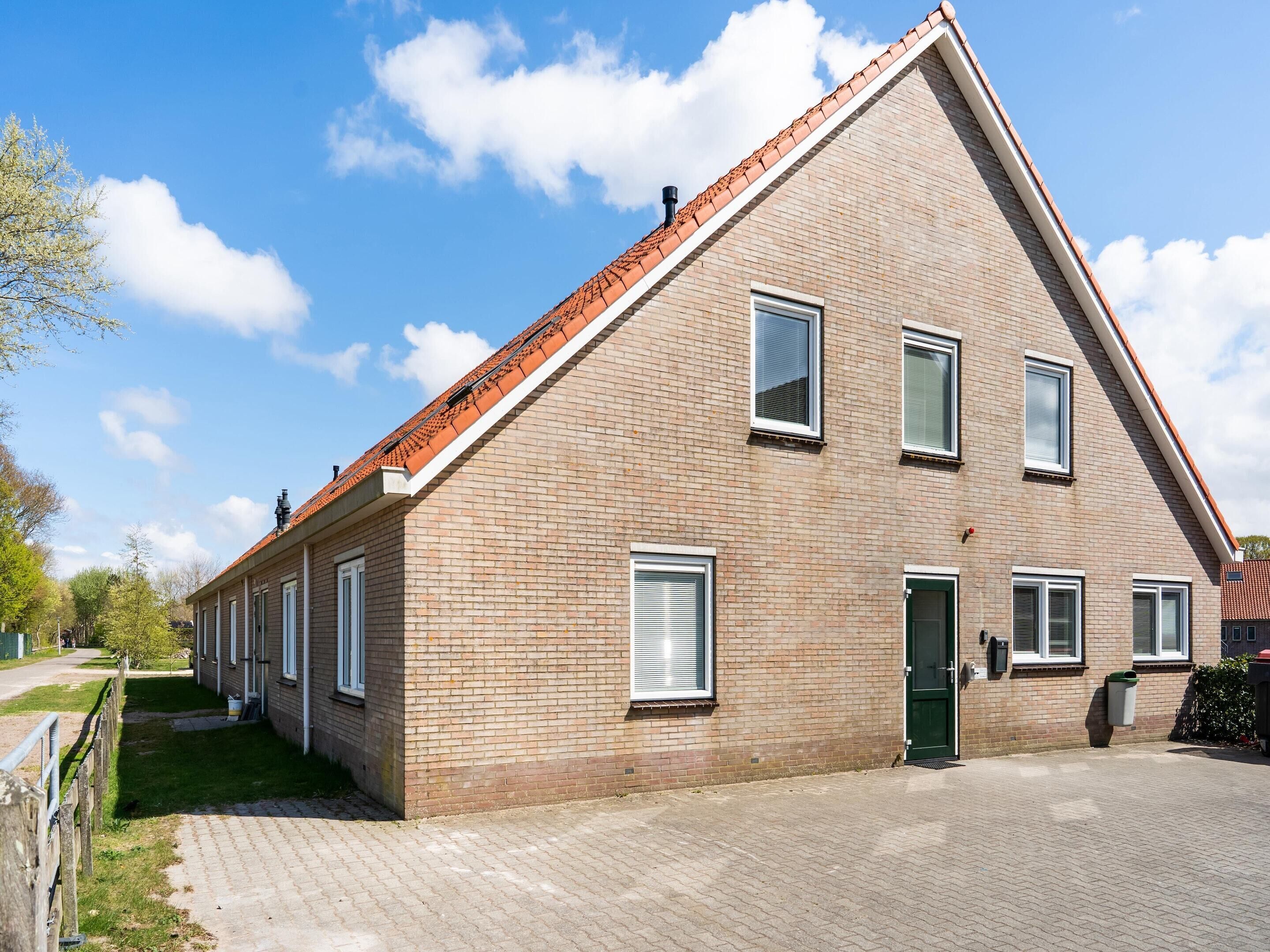 A two-story brick building with a sloped roof, multiple windows, and a paved driveway.