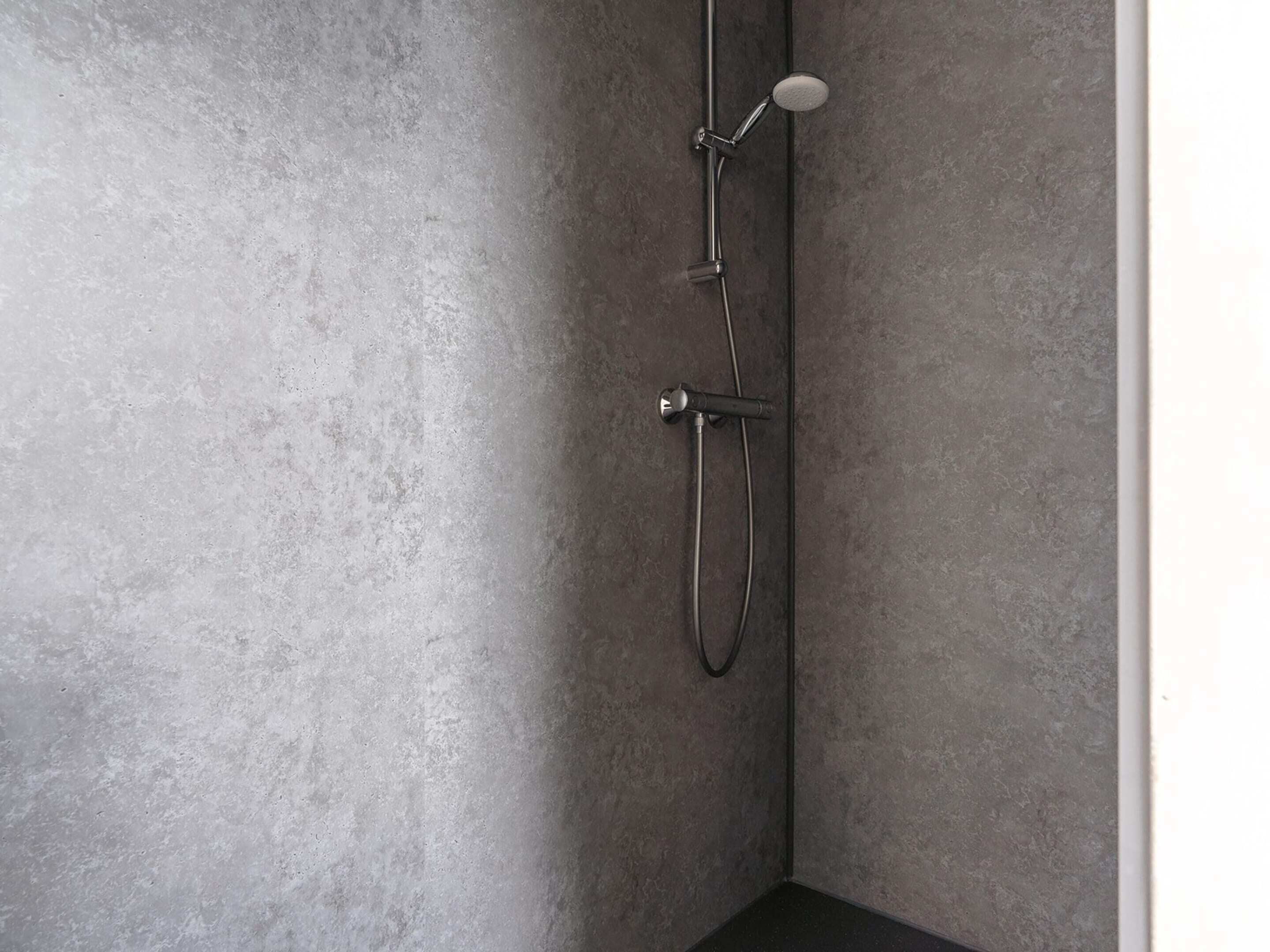 A corner of a bathroom with a shower, a handheld showerhead, and a wall-mounted faucet.