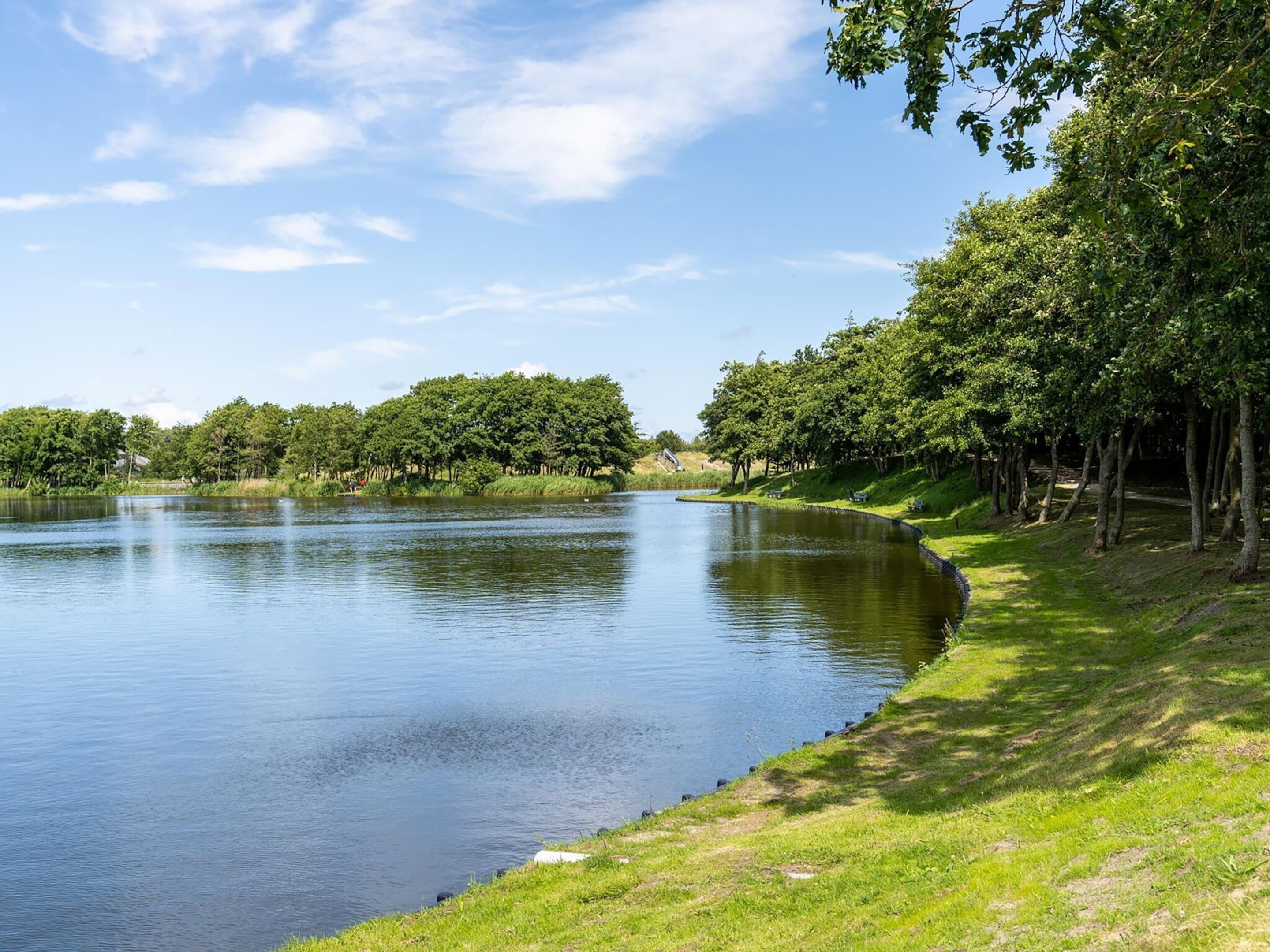 Une rivière paisible, bordée d’une rive herbeuse et d’arbres.
