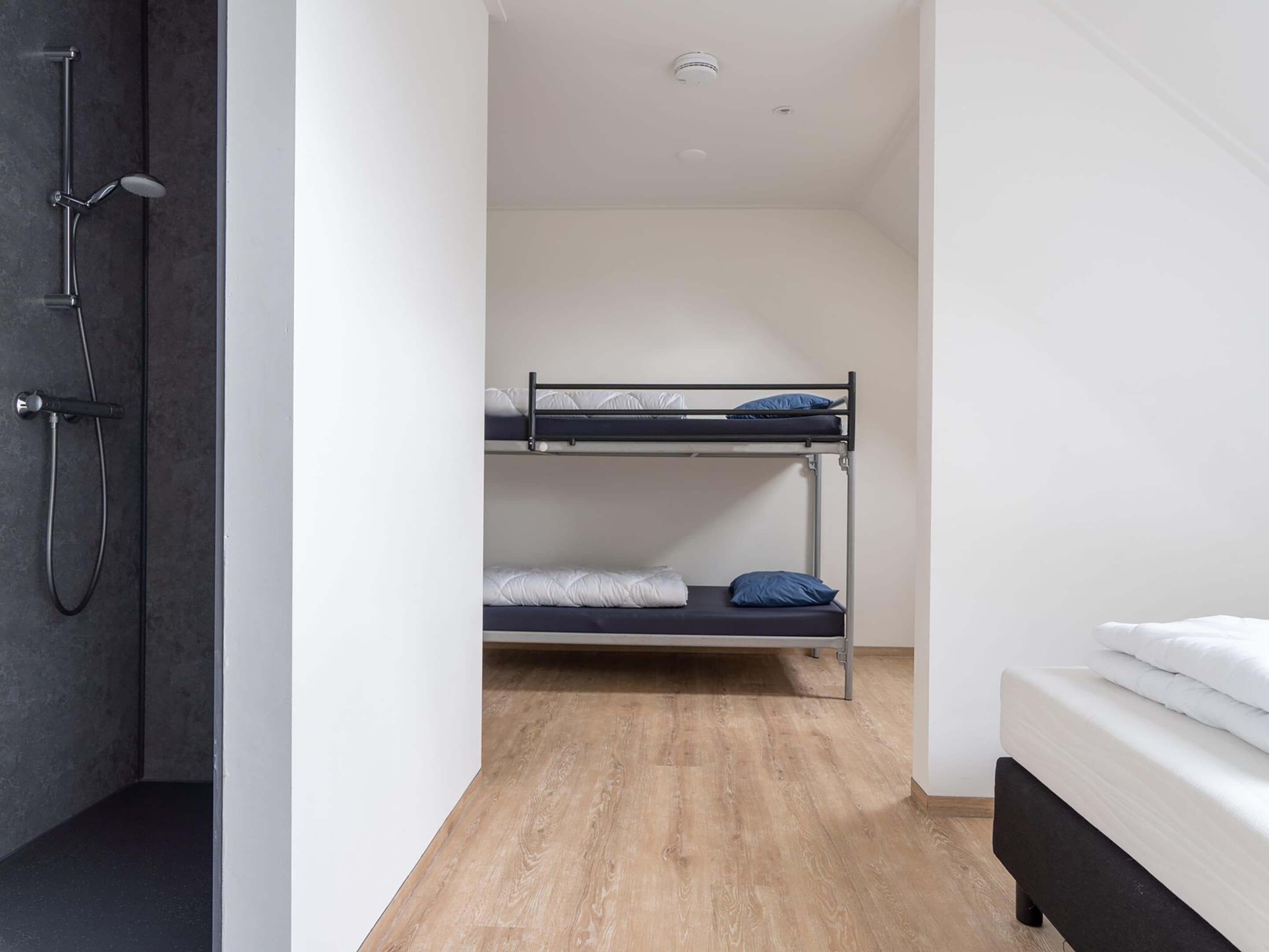 A small, modern room with a bunk bed, a shower area, and a single bed.