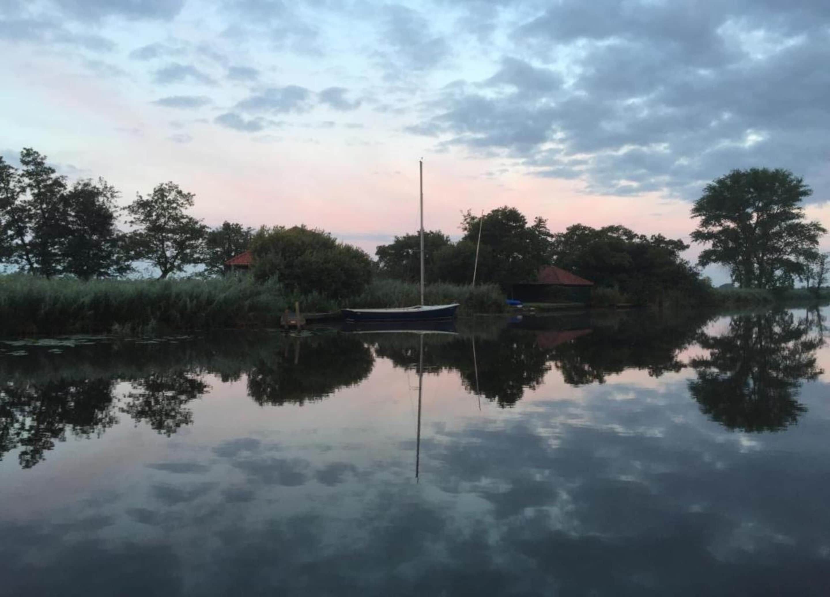 Un lago tranquilo con un bote amarrado a la orilla, rodeado de árboles y un cielo despejado.