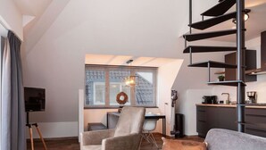 Ein modernes Wohnzimmer mit grauem Sofa, einem Couchtisch und einem Fernseher auf einem Dreibeinstativ.