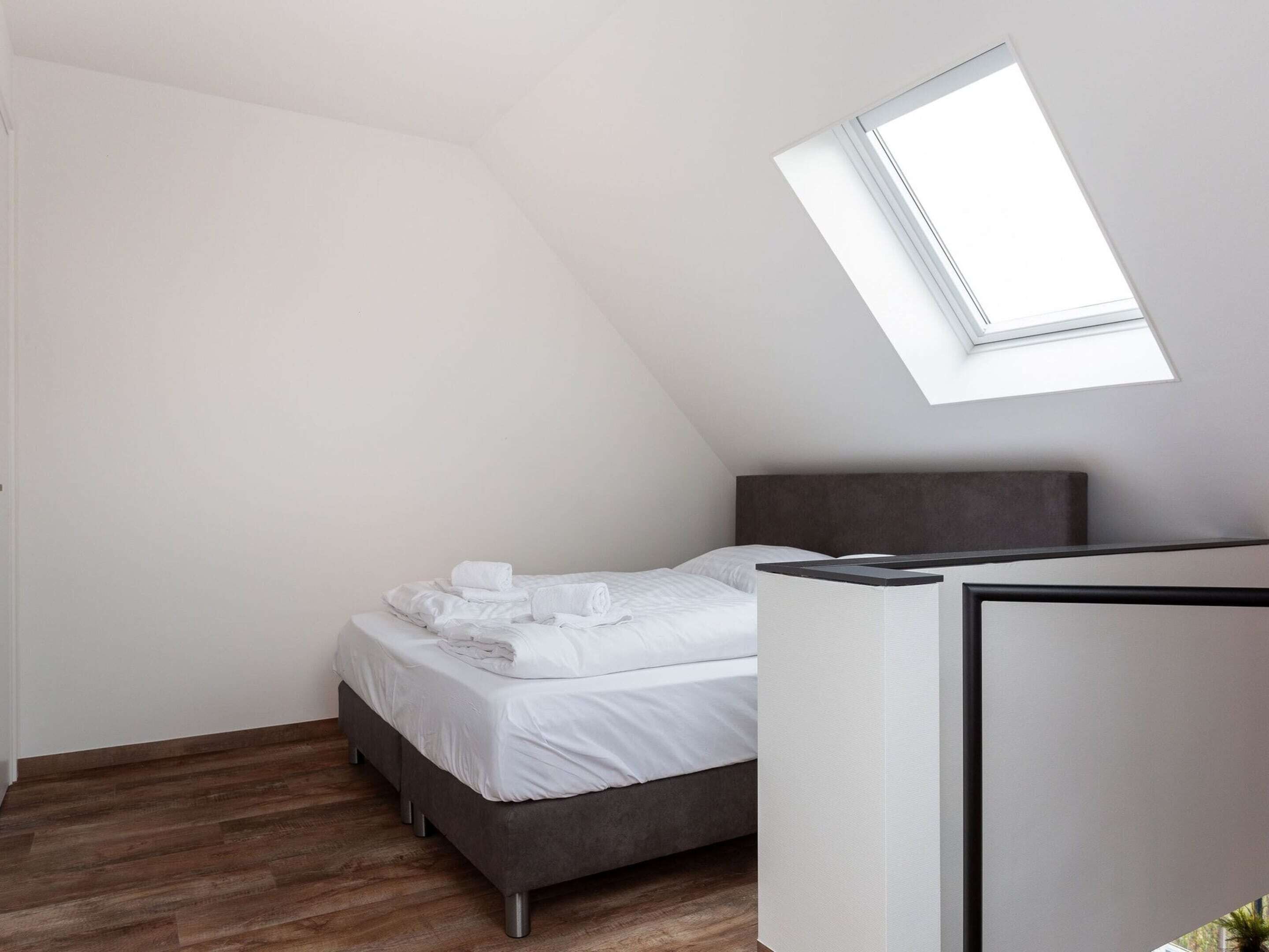 A bedroom with a skylight, a bed with white linens, and a dark headboard.