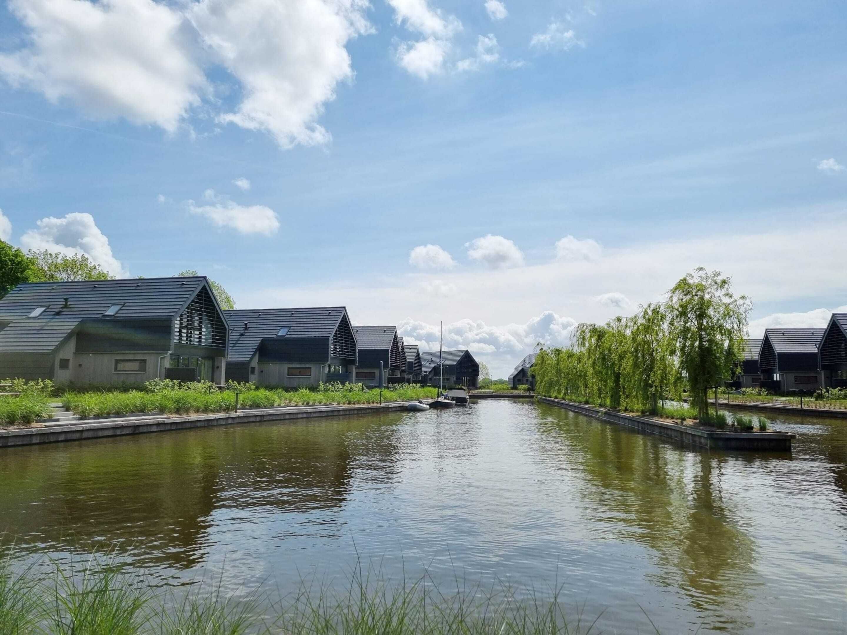 A canal with modern buildings on either side, a clear sky, and a calm water surface.