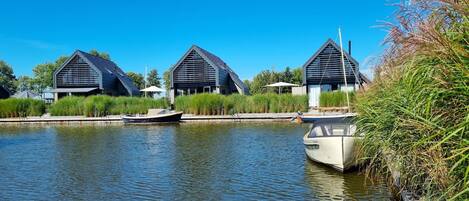 A canal with two modern buildings, a boat docked, and lush greenery.