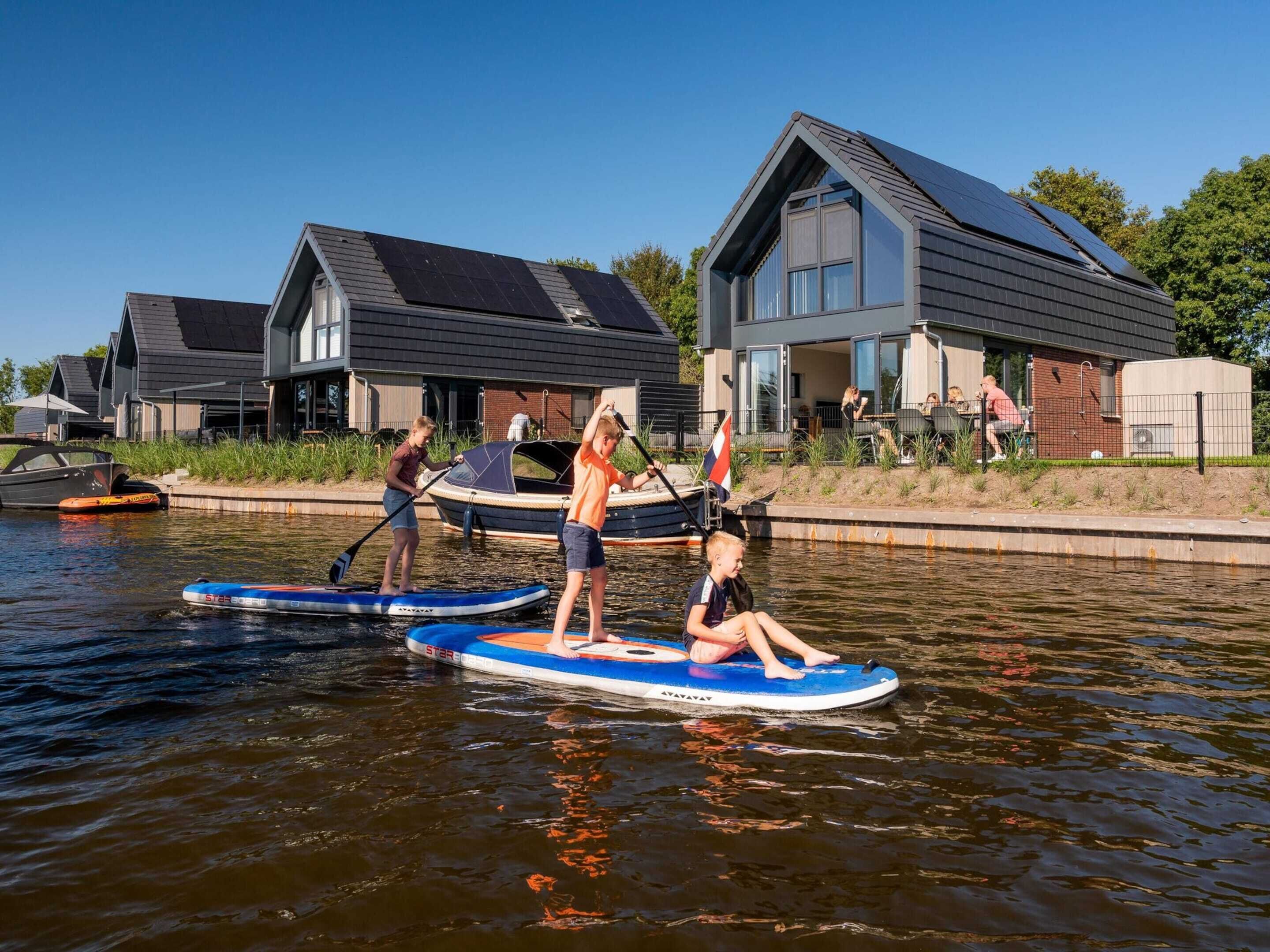 A canal with people on paddleboards, a house with a sloped roof, and a boat docked nearby.