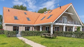 Une maison à deux étages, dotée d’un toit en pente, d’un balcon et d’un chemin de gravier menant à une table de pique-nique.