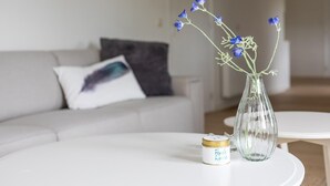 Un salon avec un canapé blanc, une petite table ronde et un vase transparent contenant des fleurs bleues.