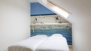 Une chambre à coucher avec un lit, une lucarne et une fresque représentant une scène de plage.