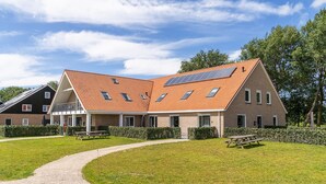 Un bâtiment moderne doté d’un toit en pente, de nombreuses fenêtres et d’un chemin pavé menant à un espace de pique-nique.