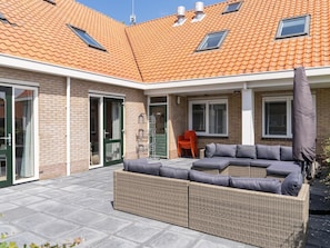 A covered patio area with a sectional sofa, a small table, and a chair.