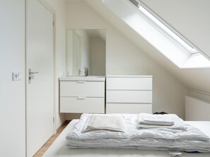 A bedroom with a skylight, a white wardrobe, and neatly folded towels on the bed.